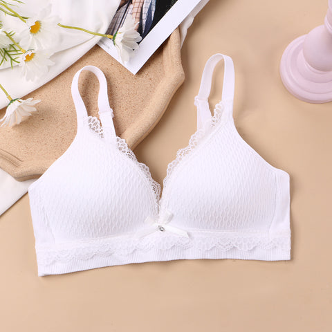 white wireless bralette with delicate lace knit design and a center bow, offering a youthful and comfortable lingerie option, presented in a serene setting with white daisies and elegant accessories.